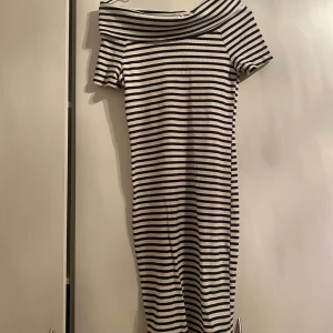 Randig klänning med offshoulder - Säljer en superfin randig klänning i marinblått och vitt. Den har en snygg offshoulder-design och korta ärmar, perfekt för sommardagar. Materialet känns mjukt och bekvämt, och passformen är normal. Perfekt för en avslappnad dag på stan eller en sommarfest!