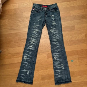 Låga jeans med slitningar från Zinnia - Säljer ett par mörkblå jeans från Zinnia i storlek XS. De har coola slitningar och ett unikt mönster längs benen. De är utsvängda och låga i midjan!