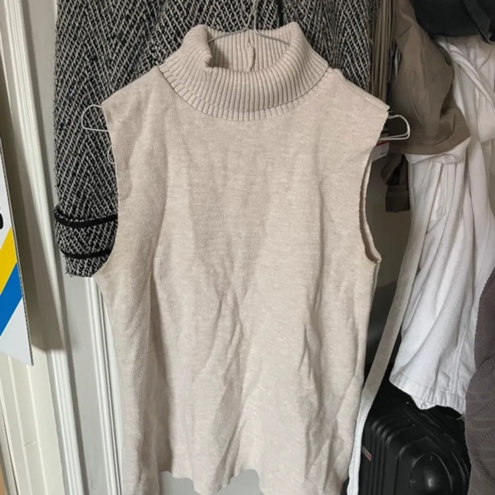 Säljer en superfin beige ärmlös polotröja i mjukt material. Perfekt för lager-på-lager under hösten eller våren. Den har en hög polokrage som ger en stilren look. Passar både till vardags och lite mer uppklädda tillfällen. 🧶✨. Tröjor & Koftor.