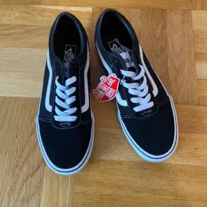 Säljer ett par klassiska svarta Vans sneakers i nytt skick. De har vit snörning och den ikoniska vita sidostripen. Perfekta för både vardag och fest! Storlek är 37, i standard passform.