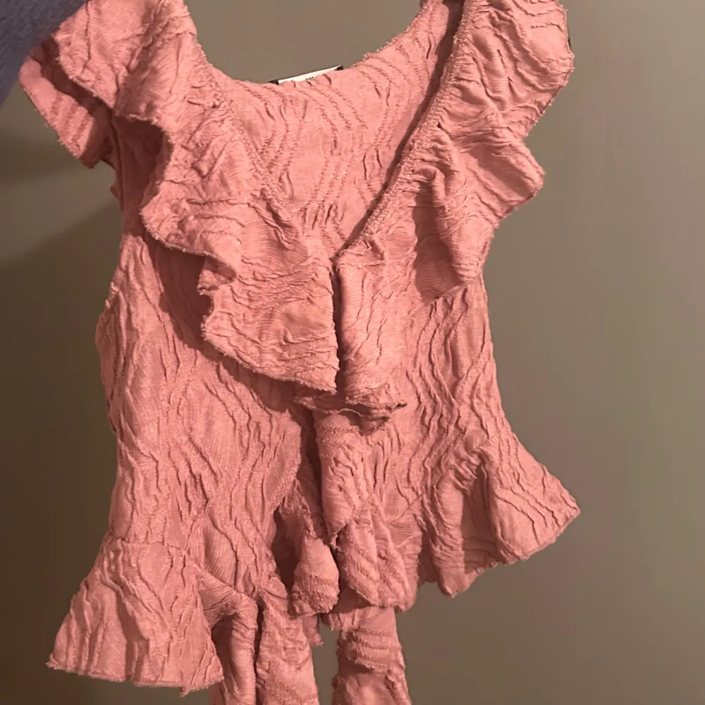 Säljer en superfin rosa topp med volanger. Den är ärmlös och har en v-ringad design som ger en romantisk känsla. Perfekt för sommardagar eller en festlig kväll. Materialet är lätt och luftigt, vilket gör den bekväm att bära. Passar perfekt med jeans eller kjol för en chic look!. Yläosat.