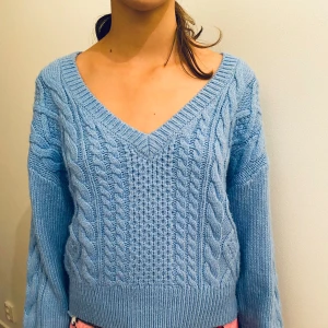 Ljusblå stickad tröja med flätmönster strlk 170 - Superfin ljusblå stickad tröja med v-ringning och snyggt flätmönster. Perfekt för kyliga dagar och ger en mysig känsla. Tröjan har långa ärmar och ribbade kanter som håller värmen inne. Passar perfekt till både jeans och kjol! Personen på bilden har normalt strlk 158/164