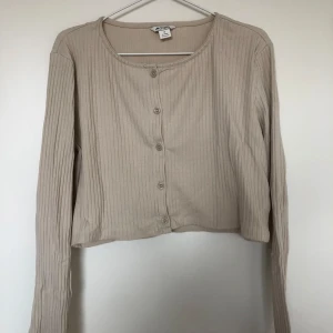 Långärmad croppad beige tröja från Monki - Beige, långärmad och croppad tröja med knappar framtill från Monki. Välanvänd men fortfarande i fint skick.