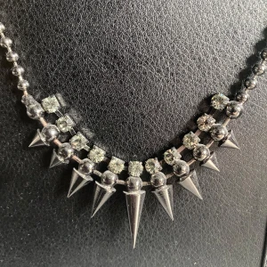 Punkhalsband med Nitar - Köpte halsbandet för många år sedan och har inte använt den mycket sen dess. Väldigt fint skick, mörk sliver/svart metall med vita stenar