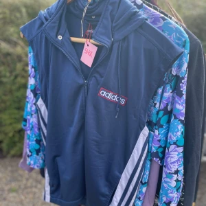 Blå Adidas väst - Säljer en retro blå Adidas väst. Den är i bra skick och har en avslappnad passform. Perfekt för en sportig look eller chill häng!