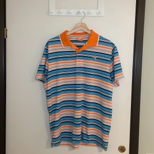Randig pikétröja från Puma - Säljer en färgglad randig pikétröja från Puma i storlek M. Tröjan har en fräsch mix av blå, orange och vit med en klassisk krage och knappar framtill. Perfekt för sommardagar eller en avslappnad dag på stan. 🧡💙Pris går alltid att förhandlas!