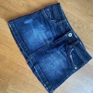 Mörkblå jeanskjol - Säljer en snygg mörkblå jeanskjol i bra skick. Den har coola sömmar på bakfickorna. Perfekt för sommardagar eller en avslappnad utekväll. Kjolen är kort och har en knapp och dragkedja framtill. På kjolens framsida är det slitna detaljer. Men inget sönder. Storleken är 146 men skulle säga ca xxs. Passar perfekt med en t-shirt eller en söt topp!