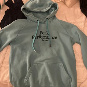 Grön hoodie från Peak Performance - Säljer en snygg och bekväm grön hoodie från Peak Performance. Den har en klassisk design med logga på bröstet och en praktisk magficka. Perfekt för kyliga dagar eller mysiga hemmakvällar. Huvan har dragsko för justerbar passform.