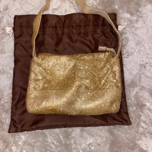 Glittrig guldväska från Bianca x Nelly.com - Säljer en superfin glittrig guldväska från Bianca x Nelly.com. Perfekt för fest eller nyår! Väskan har en dragkedja och är i mycket bra skick. Den kommer med en praktisk brun förvaringspåse. Använt denna en gång, sedan dess har den legat i sin dustbag. 