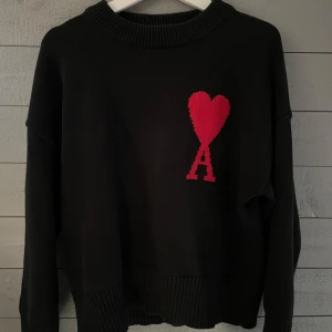 Svart stickad tröja med rött hjärta - Säljer en snygg tröja från ami paris. Sparsamt använd och i bra skick. Skriv vid minsta lilla fråga!