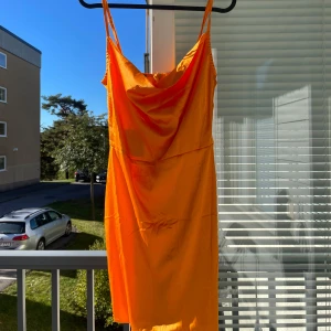 Orange axelbandslös klänning - Säljer en superfin orange klänning med smala axelband. Den är perfekt för sommardagar och har en härlig, livfull färg. Klänningen är i ett mjukt och lätt material, vilket gör den bekväm att bära hela dagen. Perfekt för både vardag och fest!