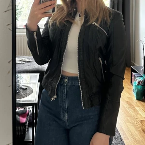 Svart skinnjacka från Rockandblue - Säljer en snygg svart skinnjacka från Rockandblue i storlek 36. Jackan är aldrig använd & det medkommer även en speciell galje till jackan om man vill ha med det . Den är fodrad med rött tyg som ger en härlig kontrast. Perfekt för höst och vår!