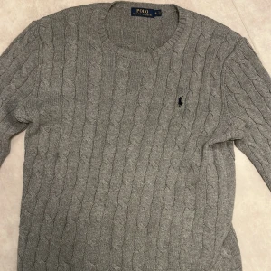 Polo Ralph Lauren Kabelstickad Tröja - En grå kabelstickad tröja gjord av Ralph Lauren, tröjan är i utmärkt skick och passar perfekt till vintern och hösten. Skriv om ni har frågor🔥🤝