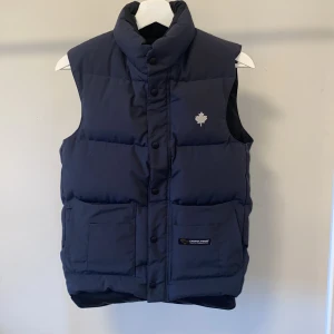 Mörkblå dunväst från Canada Goose - Säljer min knappt använda Canada Goose väst i nyskick. 💞Den är i storlek 2XS, men passar mig som brukar ha Xs/S i vanliga fall. Säljer den nu för att den inte kommer till användning. Skriv för mer bilder eller information💞