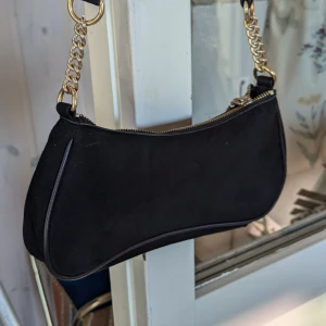 Svart axelväska med guldkedja - Säljer en snygg svart axelväska från H&M. Väskan har en elegant guldkedja som axelrem och en praktisk dragkedja upptill.I mycket fint skick