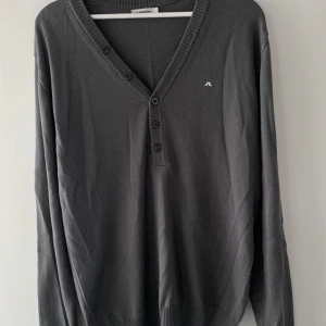 Grå tröja från J.Lindeberg - Säljer en stilren grå tröja från J.Lindeberg. Den har en v-ringad design med knappar framtill och långa ärmar. Perfekt för både vardag och lite finare tillfällen. Superbekväm och lätt att matcha med det mesta i garderoben!