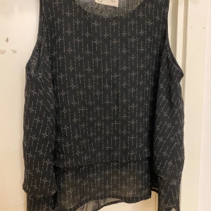 Svart mönstrad topp från Ü - Säljer ett snyggt svart Linne från Ü med ett coolt mönster i vitt. Linnet har en lös passform, och är i storlek 134.