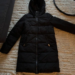 Svart pufferjacka från ONLY - Säljer en svart pufferjacka från ONLY i storlek XS. Jackan har en dragkedja framtill och är perfekt för kalla dagar. Den är långärmad och har en mysig huva för extra värme. 