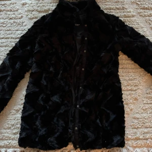 Svart pälsjacka från Vero Moda - Säljer en supermjuk och stilren svart pälsjacka från Vero Moda. Perfekt för att hålla sig varm och snygg under kyliga dagar. Jackan har knappar framtill och är helfodrad för extra komfort. 