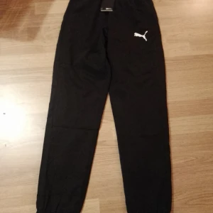 Svarta träningsbyxor från Puma helt nya ! - Snygga svarta träningsbyxor från Puma med normal passform. Perfekta för löpning och andra träningsaktiviteter. Byxorna har en elastisk midja och Puma-loggan på benet.