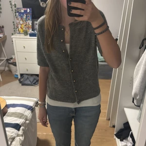 Grå kofta med guldknappar - Säljer en stilren grå kofta med korta ärmar och eleganta guldknappar. Perfekt för lager-på-lager och passar till både jeans och kjol. Ett mångsidigt plagg för alla tillfällen.