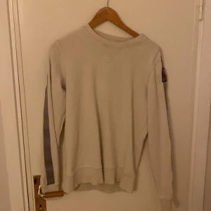 Beige fleece tröja från Parajumpers - Säljer en beige fleece tröja från Parajumpers med grå detaljer på ärmarna. Tröjan har en rund hals och ett märke på ärmen. Perfekt för kyliga dagar.