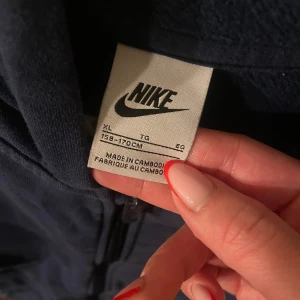 Mörkblå hoodie från Nike - Säljer en mörkblå hoodie från Nike med dragkedja och huva. Den har en klassisk design med Nike-logga på bröstet och är tillverkad i ett mjukt material för extra komfort.