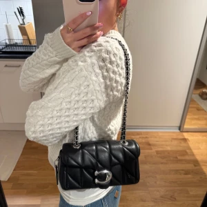 Svart quilted tabby 20 från Coach🍒 - Säljer min supersnygga svarta väska från Coach🥰Använd endast en gång! Nypris: 4855kr🌸Väskan har en stilren design med ett metallspänne framtill och en praktisk storlek för vardagsbruk. Bandet kan justeras så man kan ha väskan runt axeln eller dra ut kedjan och ha väskan rumt kroppen😇💗 Säljer endast för att jag byter till guld smycken💕Dustbag kommer med.