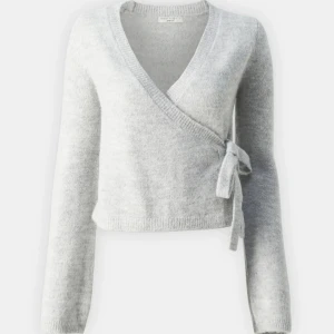 Grå omlott kofta från gina  - Säljer en stilren grå omlott kofta från gina.Den har en knytning i sidan och är tillverkad i ett mjukt material. Perfekt för lager-på-lager under kyligare dagar.