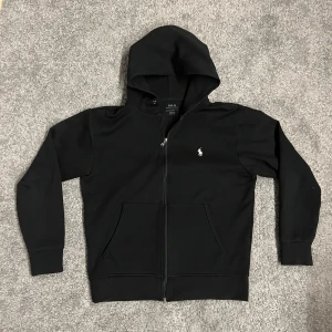 Polo Ralph Lauren Zip-Up - Säljer en stilren svart hoodie från Polo Ralph Lauren i storlek S (inte barn XL) med dragkedja och klassisk logga på bröstet. Köpare står för eventuell tillbakaskicknads kostnad. Skickas snabbt!