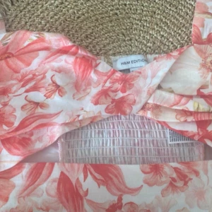 Blommig top från H&M Edition - Säljer en vacker blommig klänning från H&M Edition i ljusa och rosa toner. Klänningen har ett romantiskt mönster med blommor och en smickrande passform. Perfekt för sommarens alla tillfällen.