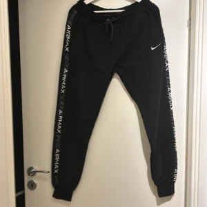 Svarta mjukisbyxor från Nike - Säljer ett par svarta mjukisbyxor från Nike med Air Max-logga längs sidorna. Byxorna har en elastisk midja med snörning och en praktisk dragkedjeficka bak. Perfekta för en avslappnad stil.