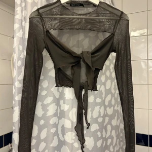 Svart mesh bolerotopp från NLY One - Trendig svart bolerotopp i mesh från NLY One. Toppen har långa ärmar och knytning framtill, vilket ger en stilfull look. Perfekt för att lägga till en extra touch till din outfit.