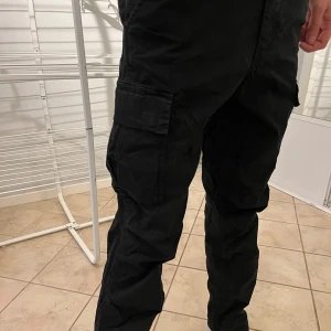 Svarta cargobyxor - Snygga svarta cargobyxor med flera praktiska fickor på sidorna. Perfekta för en avslappnad och funktionell stil. Byxorna har en normal passform och är tillverkade i ett slitstarkt material.