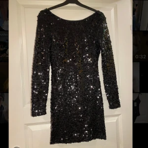 Svart paljettklänning - Snygg svart klänning täckt med glittriga paljetter. Den har en v-ringad rygg och långa ärmar, perfekt för en festlig kväll. Klänningen är kort och figurnära, vilket ger en elegant look.