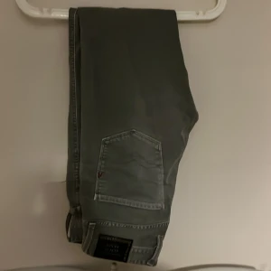 Grå jeans från Replay - Snygga grå jeans från Replay i modellen Anbass. Storlek 30/32. De har en klassisk femficksdesign med knappgylf och bälteshällor. Inga synliga märken av slitage och använt ett fåtal gånger. Pris ej hugget i sten.