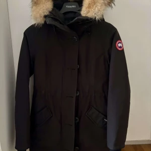  Canada Goose dam jacka - Säljer en svart parkajacka från Canada Goose med pälsdetaljer på huvan. Jackan har långa ärmar och knappar framtill. Perfekt för kalla vinterdagar. Priset går att diskutera
