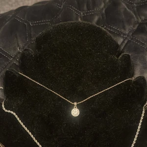 Halsband // naszyjnik - Snyggt halsband med en tunn kedja av silver och ett runt, glittrigt hängsmycke. Perfekt för att lägga till en touch av elegans till din outfit. Hängsmycket är täckt med små gnistrande stenar som fångar ljuset vackert. Säljer då den aldrig kommit till användning.