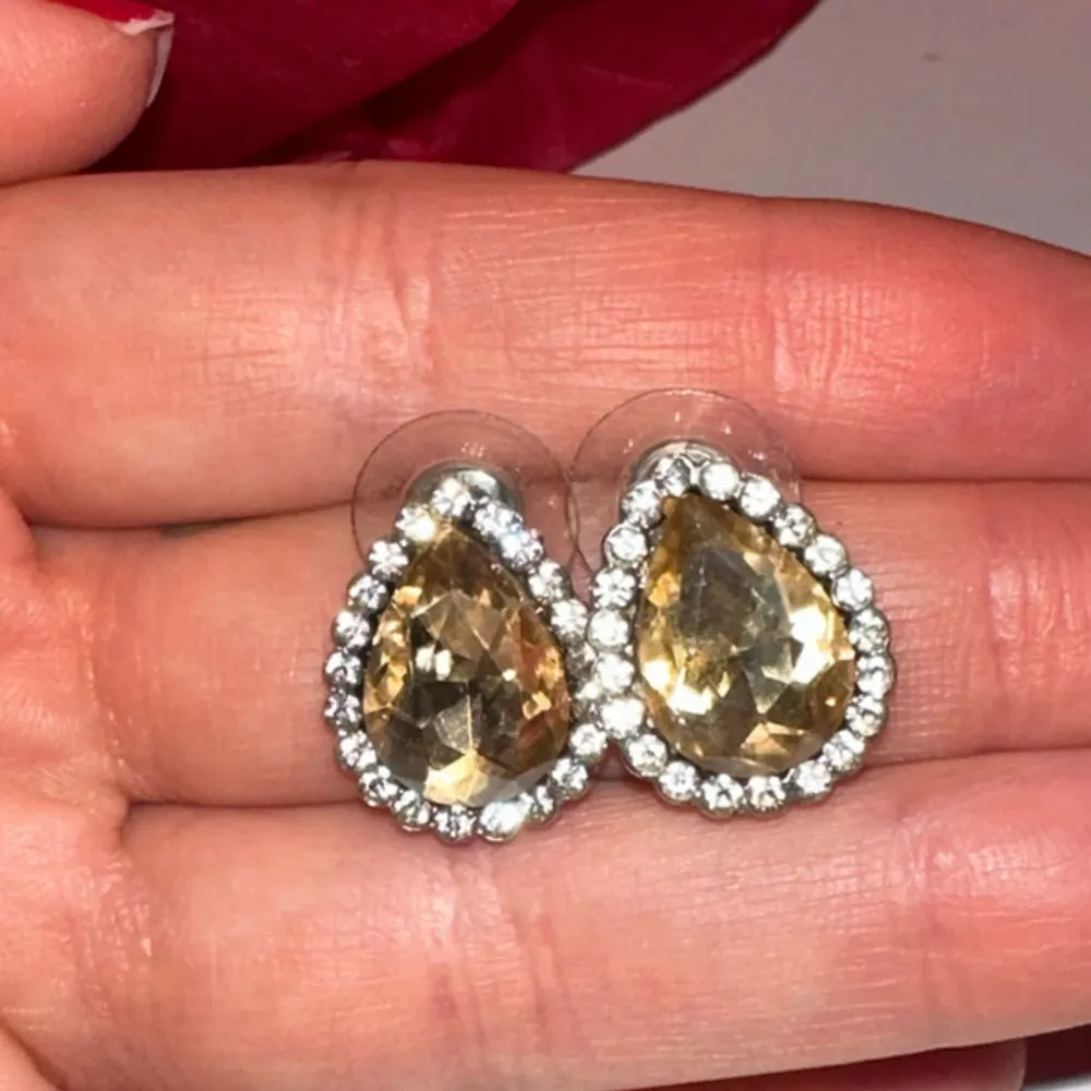 Snygga droppformade örhängen i guld med glittrande stenar runtom. Perfekta för att ge en elegant touch till din outfit. De har en klar och skimrande finish som fångar ljuset vackert.. Asusteet.