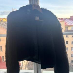 Svart pälsjacka - Snygg svart pälsjacka med en croppad design. Perfekt för att ge en lyxig touch till din outfit. Jackan har långa ärmar och en stilren look. Märke: Michael kors