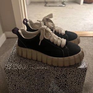 Svarta från eytys  - Snygga svarta sneakers med en kraftig  sula och vita snören. Skorna har en unik design med lila detaljer vid hälen och en mönstrad skokartong.