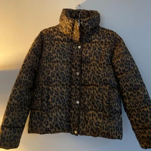 Leopardmönstrad pufferjacka från Weekday - Säljer min leopardmönstrad pufferjacka från Weekday. Jackan har en hög krage och stängs med både dragkedja och knappar. Man håller sig varm med den också där är bekväm.