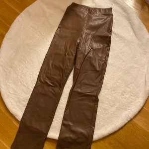 Bruna skinnbyxor från NLY Trend - Snygga bruna skinnbyxor från NLY Trend i storlek XS. Byxorna har en tight passform och är högmidjade med en praktisk dragkedja på sidan. Perfekta för en trendig look!
