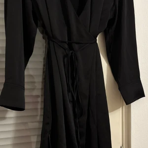 Svart omlottklänning - Elegant svart omlottklänning med långa ärmar och knytband i midjan. Perfekt för en stilren look. Om ni vill se den på, skriv gärna!