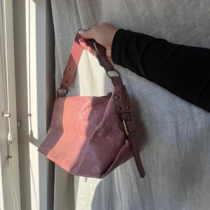 Rosa axelväska med nitar - Snygg rosa axelväska i skinn med justerbar axelrem och dekorativa nitar. Perfekt storlek. Väskan har en praktisk dragkedja för säker förvaring.