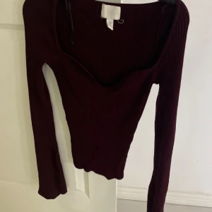 Vinröd ribbad tröja - Snygg vinröd ribbad tröja med v-ringning och långa ärmar. Perfekt för en stilren look.