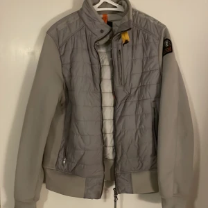 Grå  jacka från Parajumpers - Snygg grå quiltad jacka från Parajumpers med dragkedja och hög krage. Jackan har långa ärmar och ribbade muddar. Perfekt för kyligare dagar med sin stilrena design och praktiska fickor.