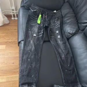 Svarta jeans från Dsquared2 - Snygga svarta jeans från Dsquared2 med slitna detaljer och vita färgstänk. De har en dragkedja och en grön etikett med märkesnamnet. Dom är för små för mig och det är anledningen till varför jag säljer. Priset kan sänkas