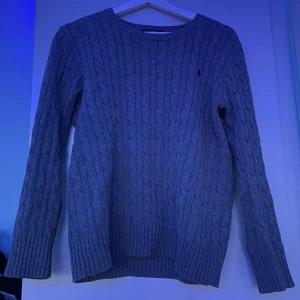 Grå stickad tröja från Polo ralph lauren - Säljer en stilren grå stickad tröja från Polo ralph luren med kabelstickat mönster. Tröjan har långa ärmar och ribbade muddar vid ärmslut och nederkant. Perfekt för kyliga dagar. 