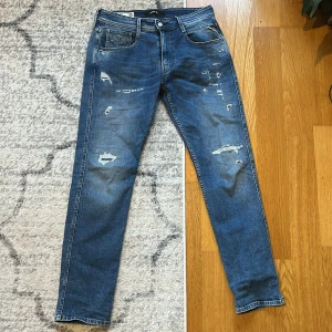Replay Anbass - Snygga blå jeansbyxor från Replay Anbass med slitna detaljer och slim fit. Perfekta för en avslappnad stil med en modern touch. Midwaist design och klassisk femficksmodell. 32/32